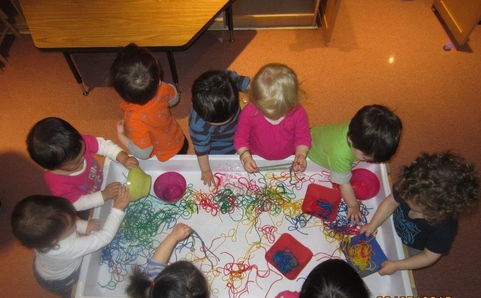 Nine children around a table playing with colourful string.
