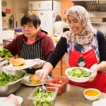 A Chinese senior and staff person are serving salad and hamburgers in the community lunch program