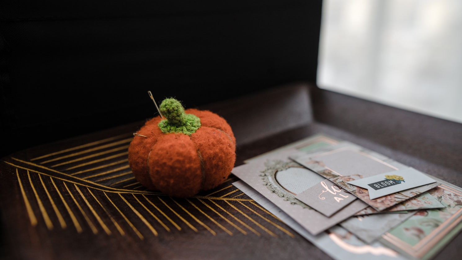 A pincushion shaped as a pumpkin is next to scrapbook paper art supplies