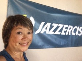 Jazzercise instructor Cheryl Hallman smiling in front of a Jazzercise banner.