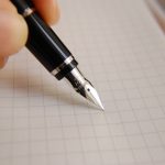 A black fountain pen is pressed against a grid paper