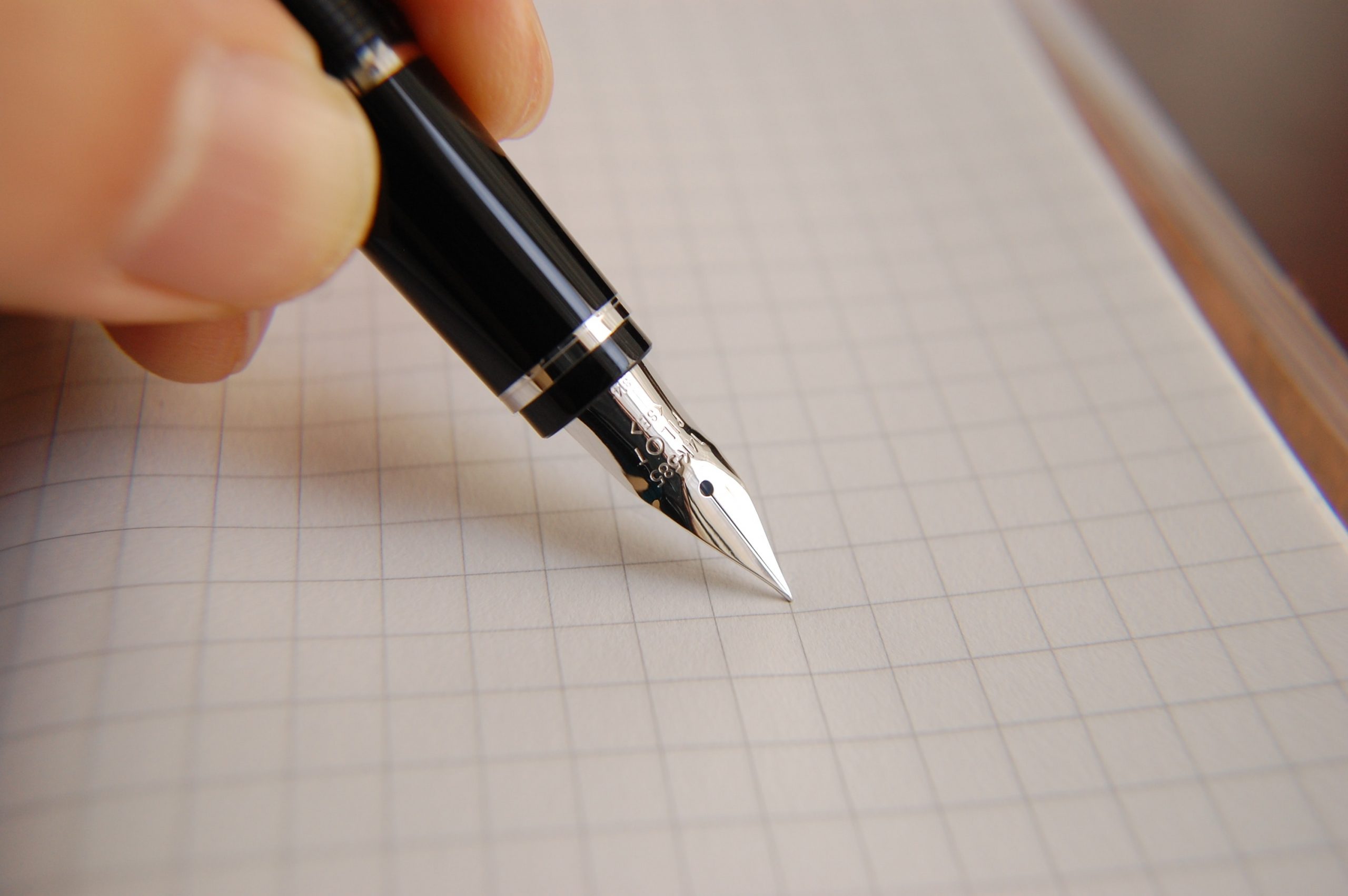 A black fountain pen is pressed against a grid paper