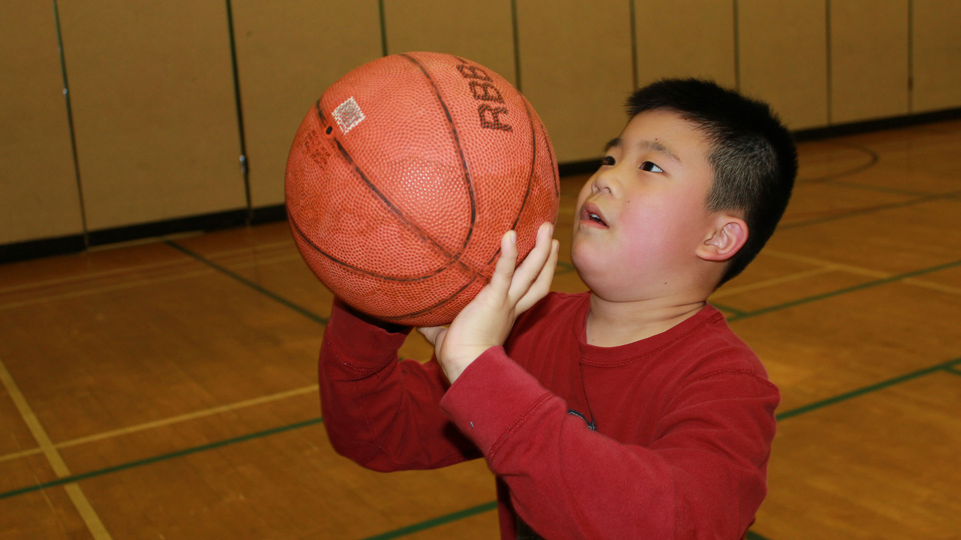 A young boy holds a basketball close to his face as he aims to throw it