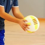 A pair of hands holds a volleyball inside a gym