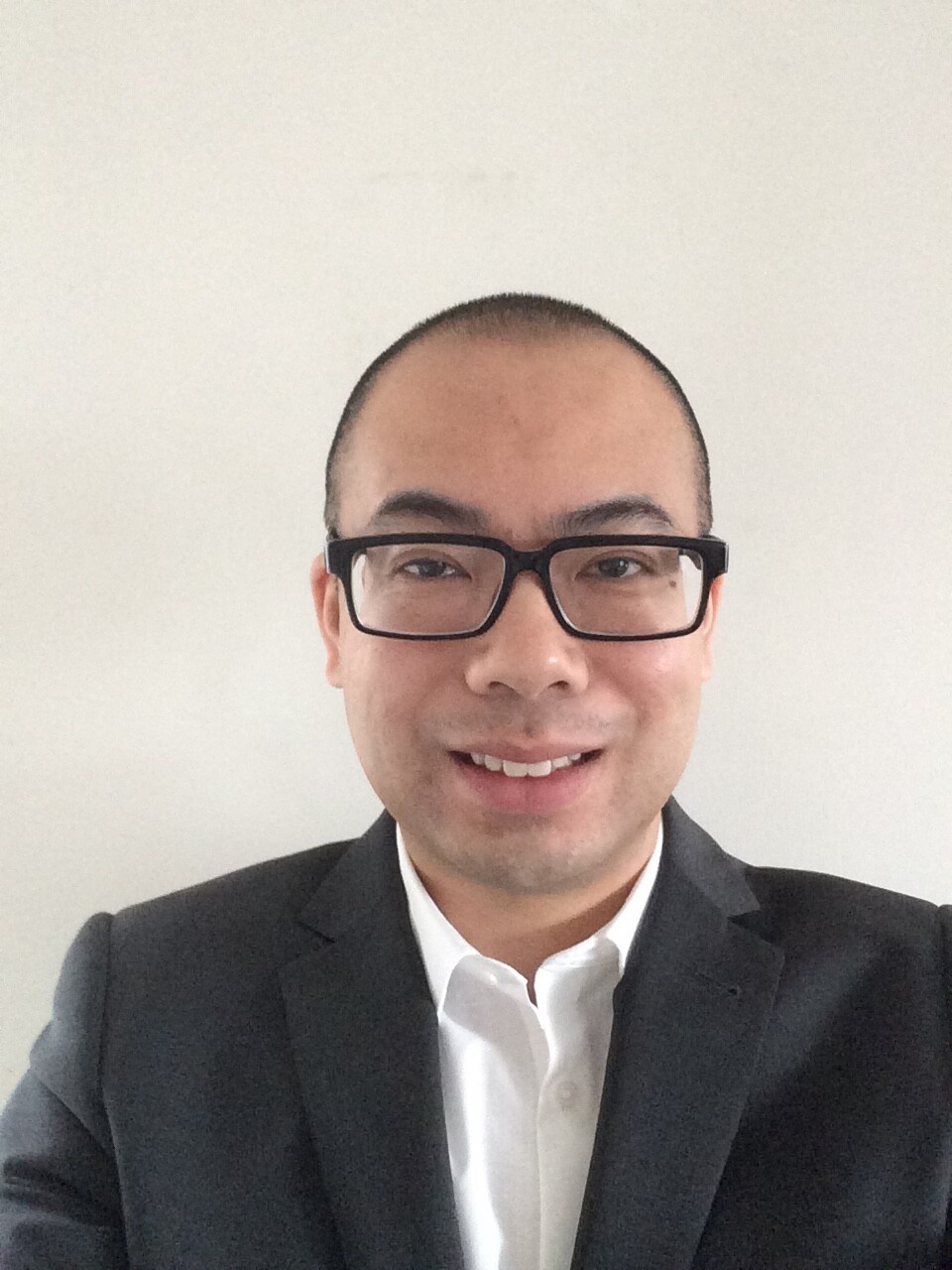 A close-up of a man wearing glasses and a dark blazer with white shirt smiling towards the camera