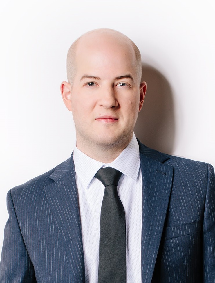 A close-up of a bald man wearing a dark blue blazer, white dress shirt and dark tie