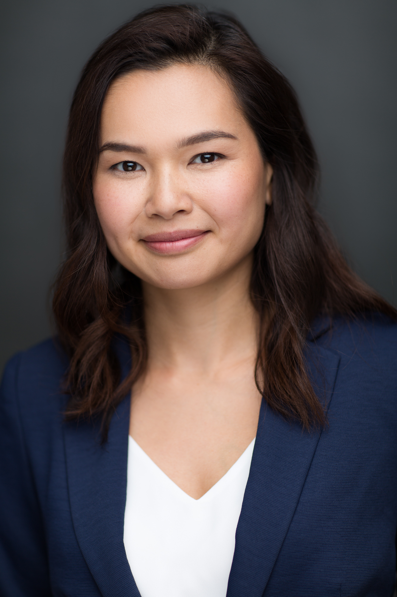 A close-up of a woman with long dark hair wearing a dark blue blazer and a white shirt