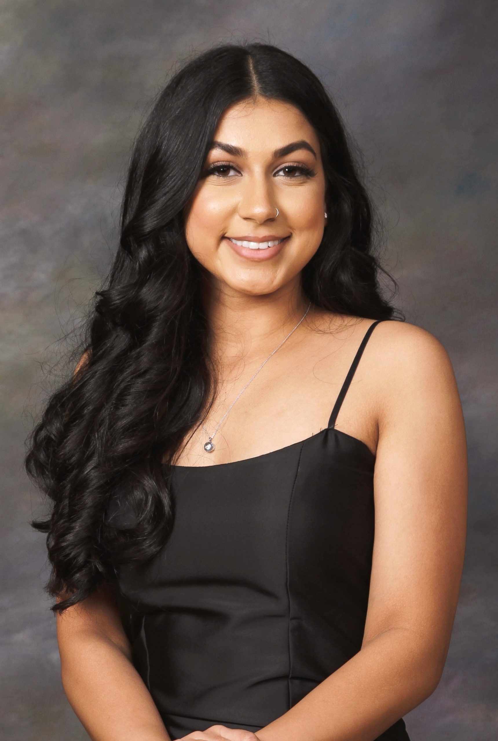 A close-up of a woman with long dark hair wearing a black dress smiling toward the camera