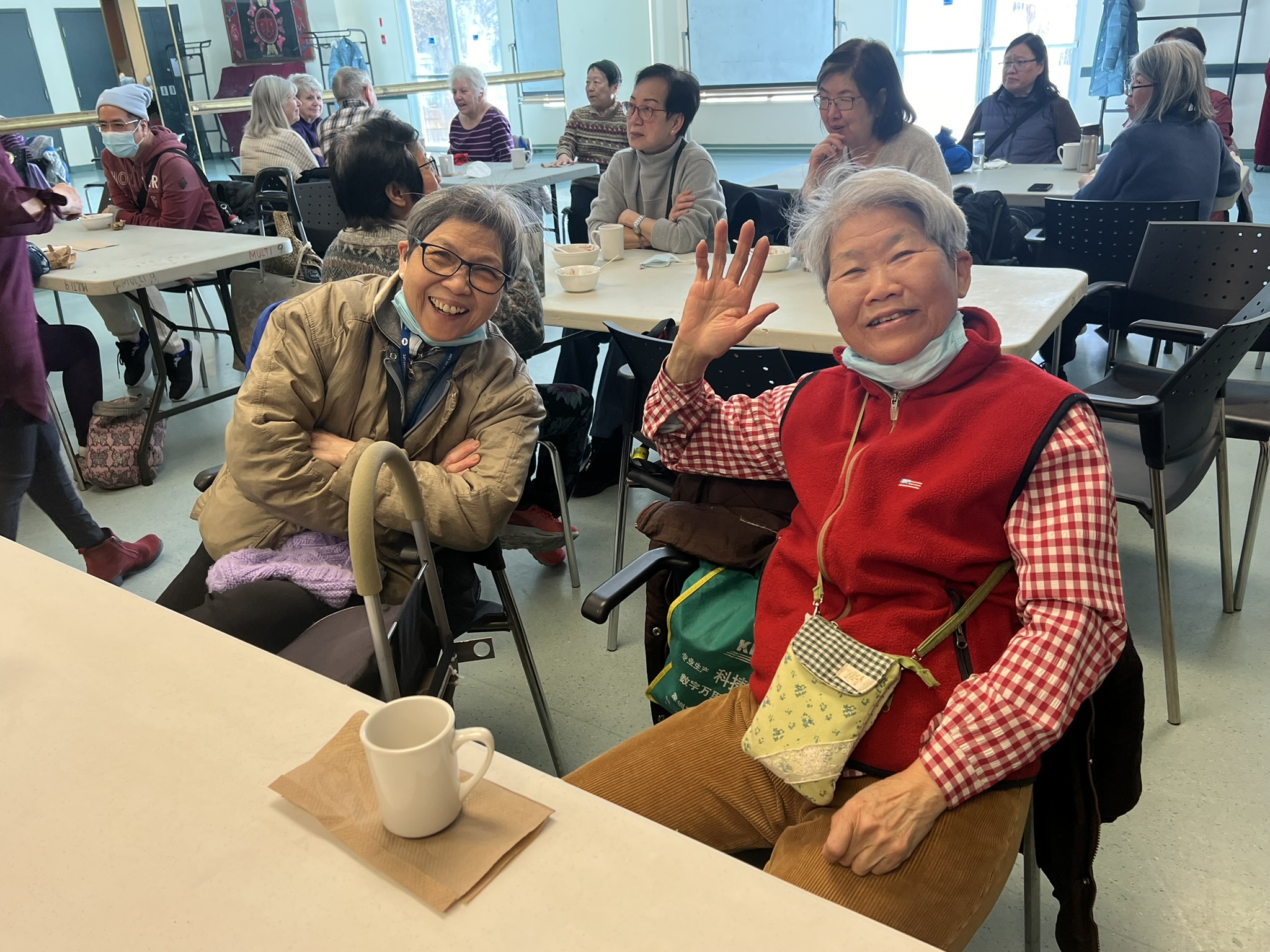 Two seniors smile towards the camera as they sit at a table inside the multipurpose room at CNH