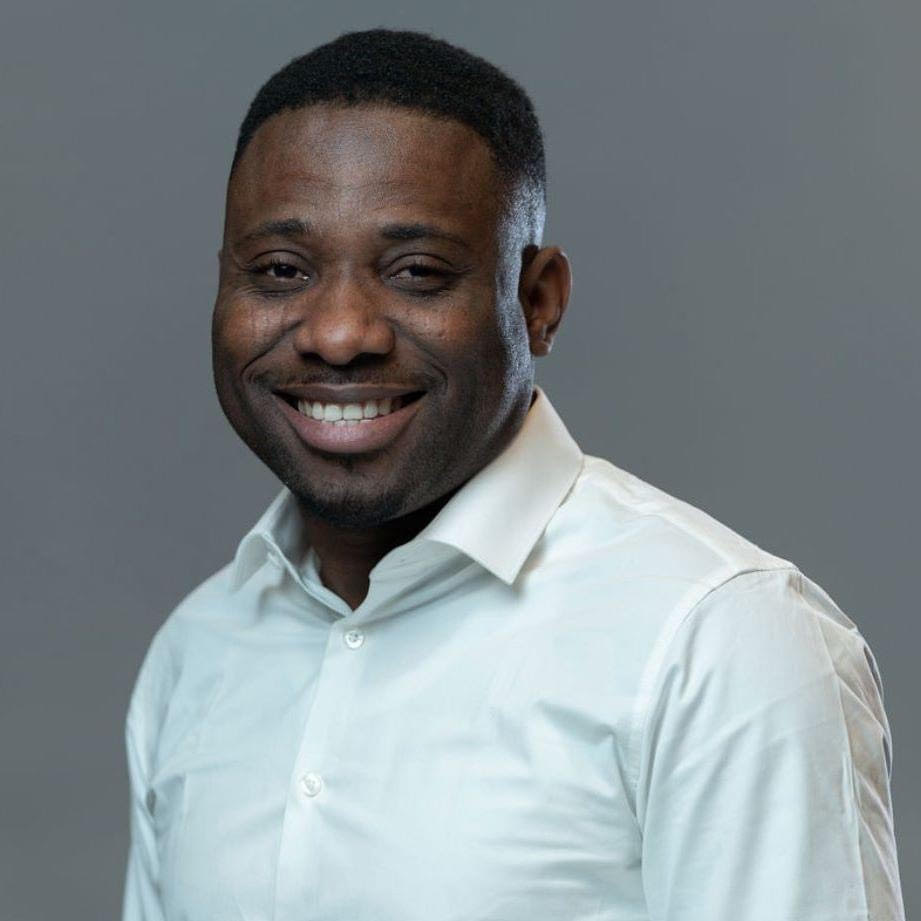 A close-up of a man with short dark hair wearing a white collared shirt smiling toward the camera