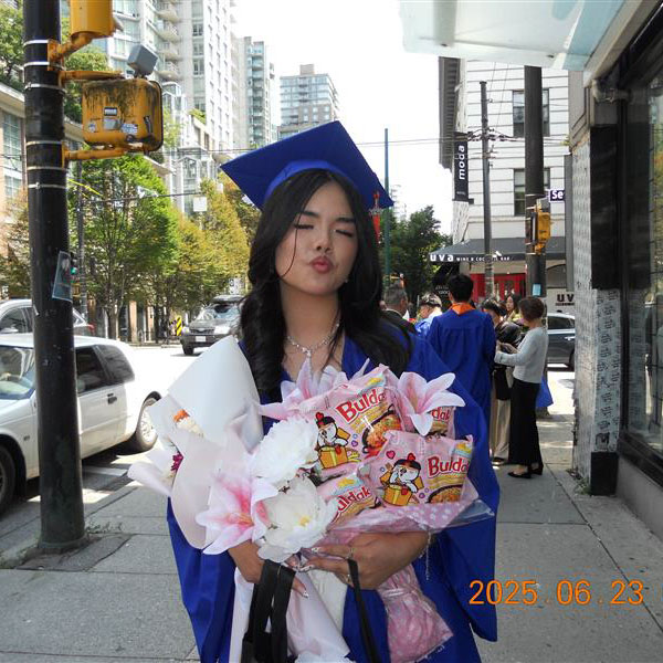 Sarah Yeung wears a blue graduation cap and gown while holding a bouquet of Baldak instant noodles packed in pink