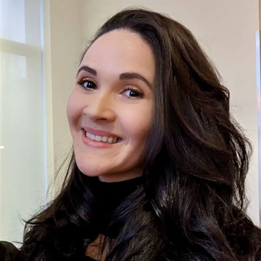 A close-up of a woman with long wavy brown hair smiling towards the camera