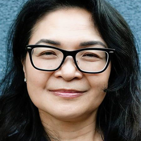 A close-up of a woman with shoulder-length black hair and dark-framed glasses.