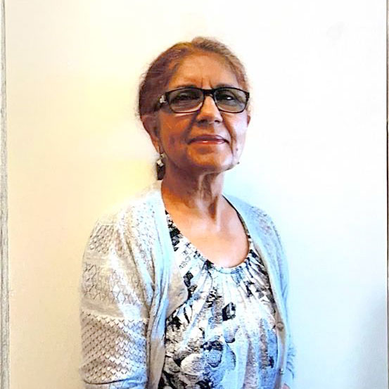 A woman with brown hair pulled back into ponytail. She is wearing glasses and a grey cardigan over floral blouse.