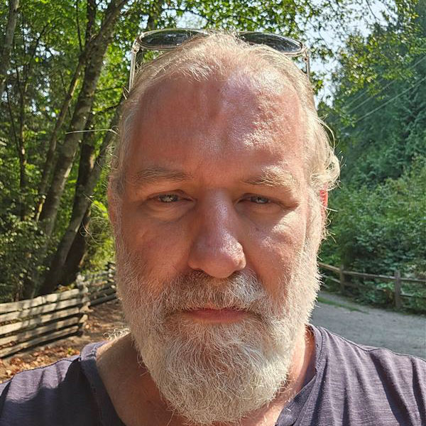 A close-up of a man with white hair and a white beard looking into the camera
