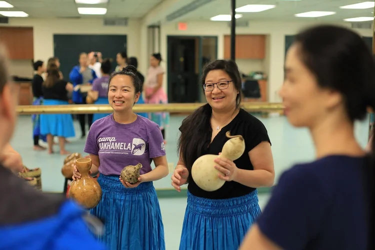 Two people stand inside a program room at CNH holding instruments made from gourds