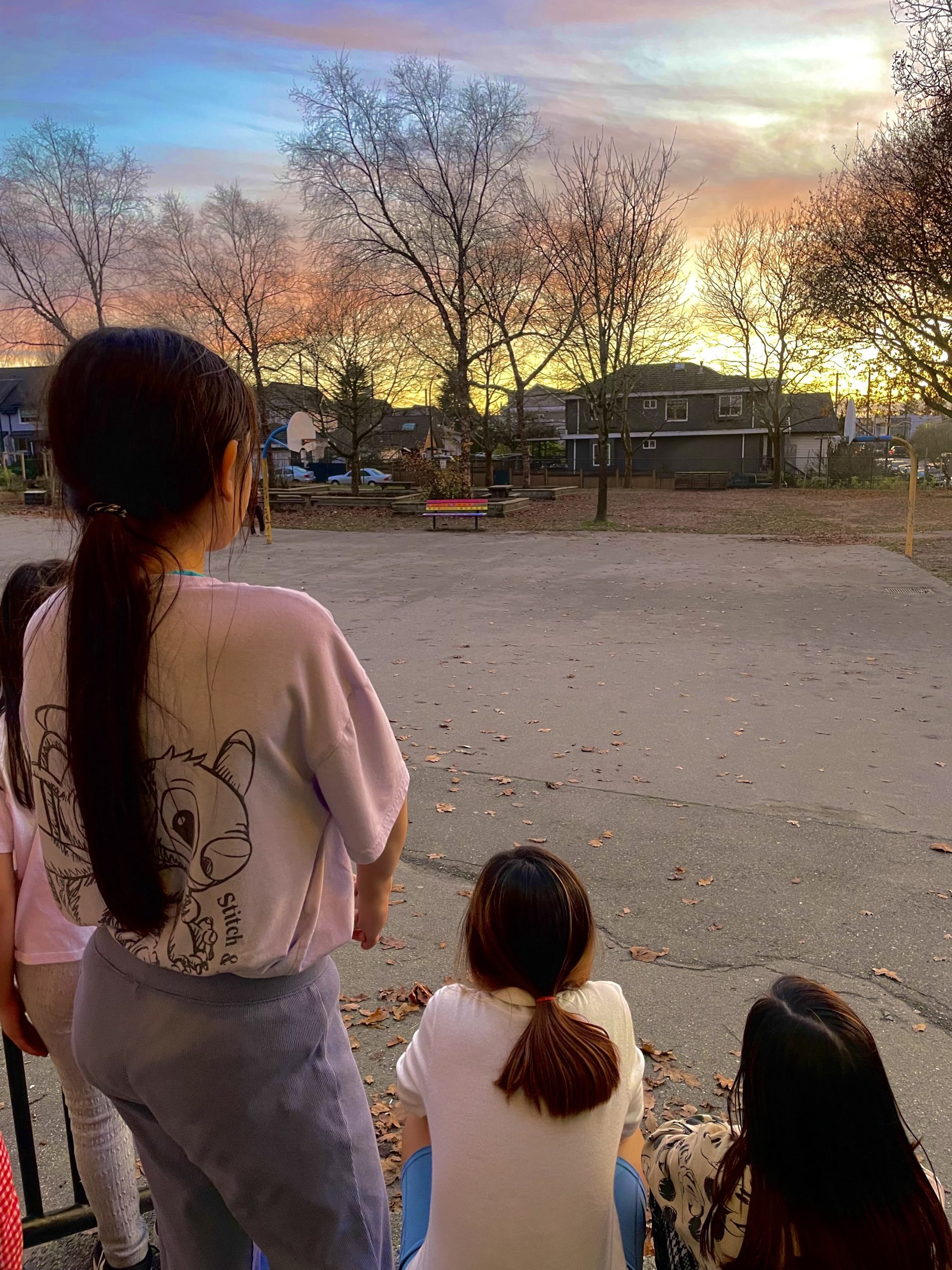 Three teenagers stand with their backs towards the camera. They look into the distance towards sunset