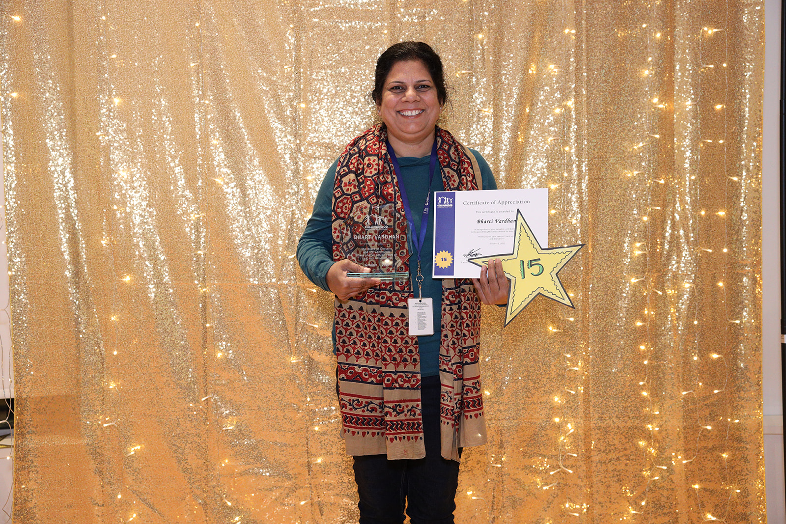 A woman stands in front of a golden backdrop holding a paper certificate and a yellow star that says, "15"