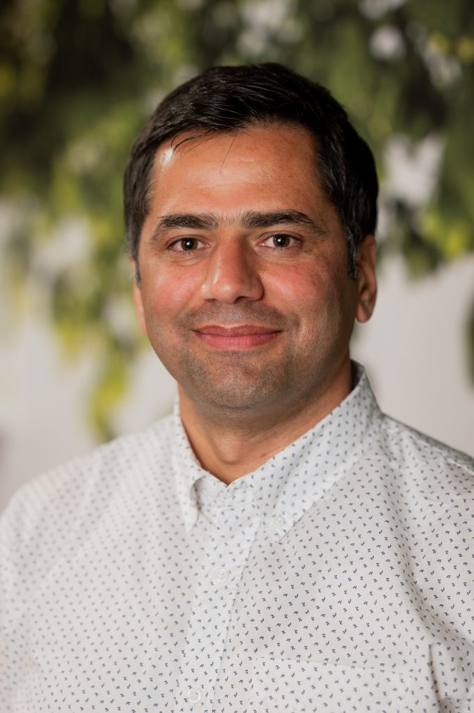 A headshot of a man smiling in a white button up shirt