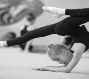 A young girl doing rhythmic gymnastics. She is upside down and balancing on her forearms and her legs are arranged into the splits